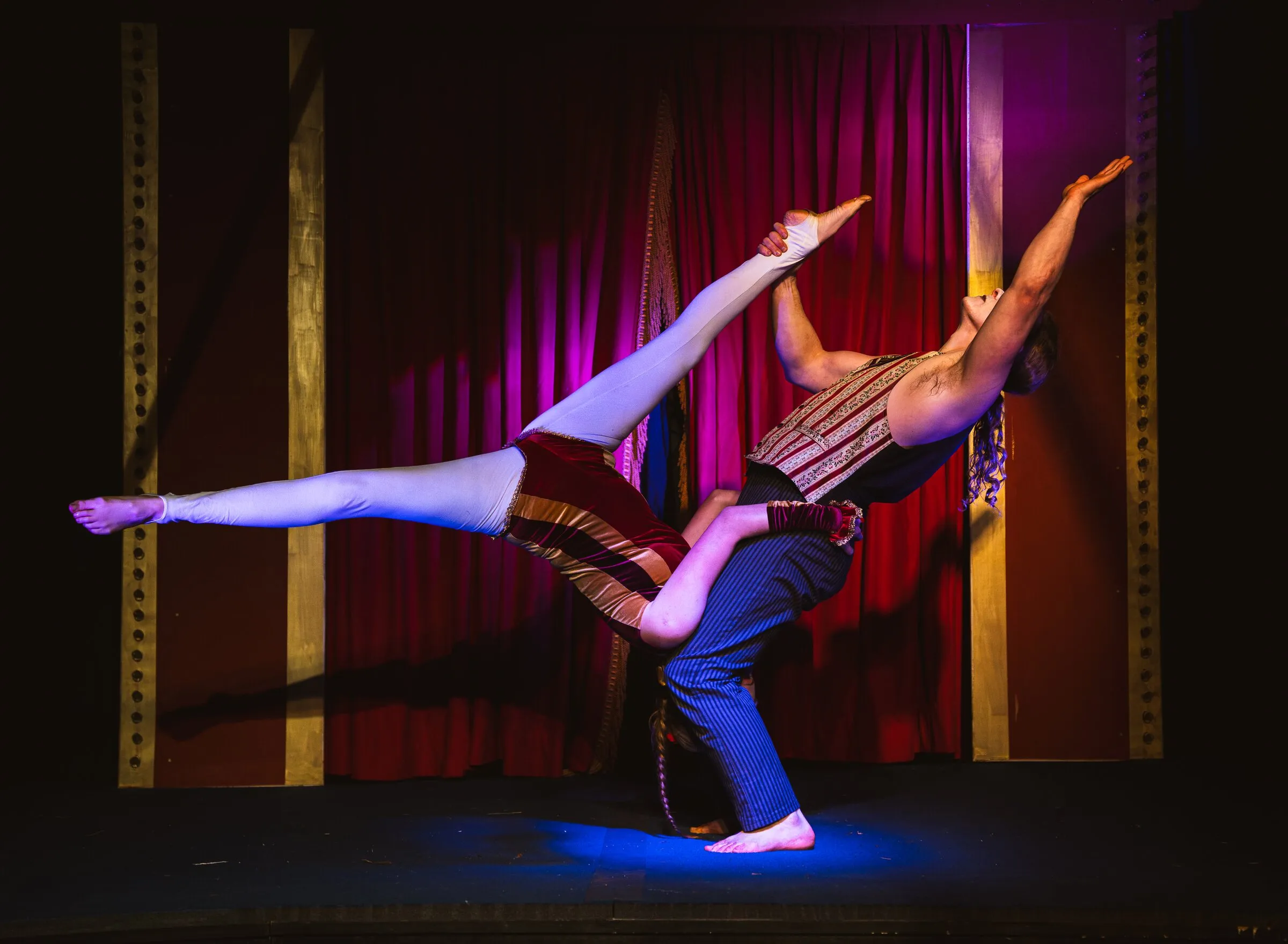 A Kuroneko Circus acrobat carrying his partner low across the stage with her legs extended