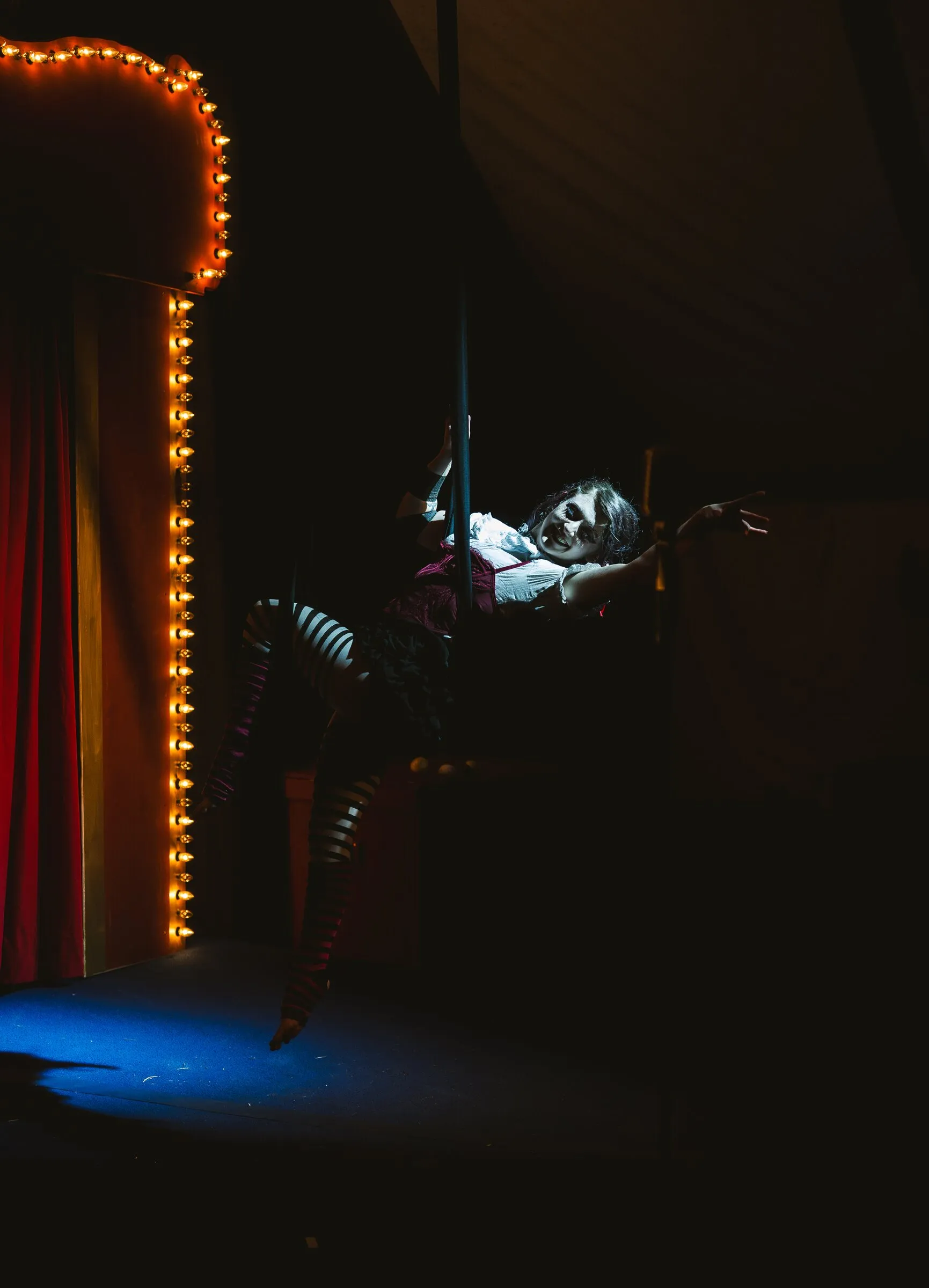 A Kuroneko Circus aerialist reclining in aerial loops high beside the marquee lights