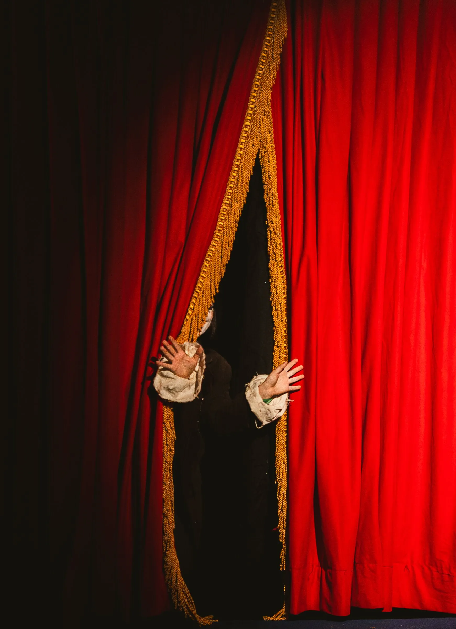A Kuroneko Circus clown parting the red curtain to peek out at the audience