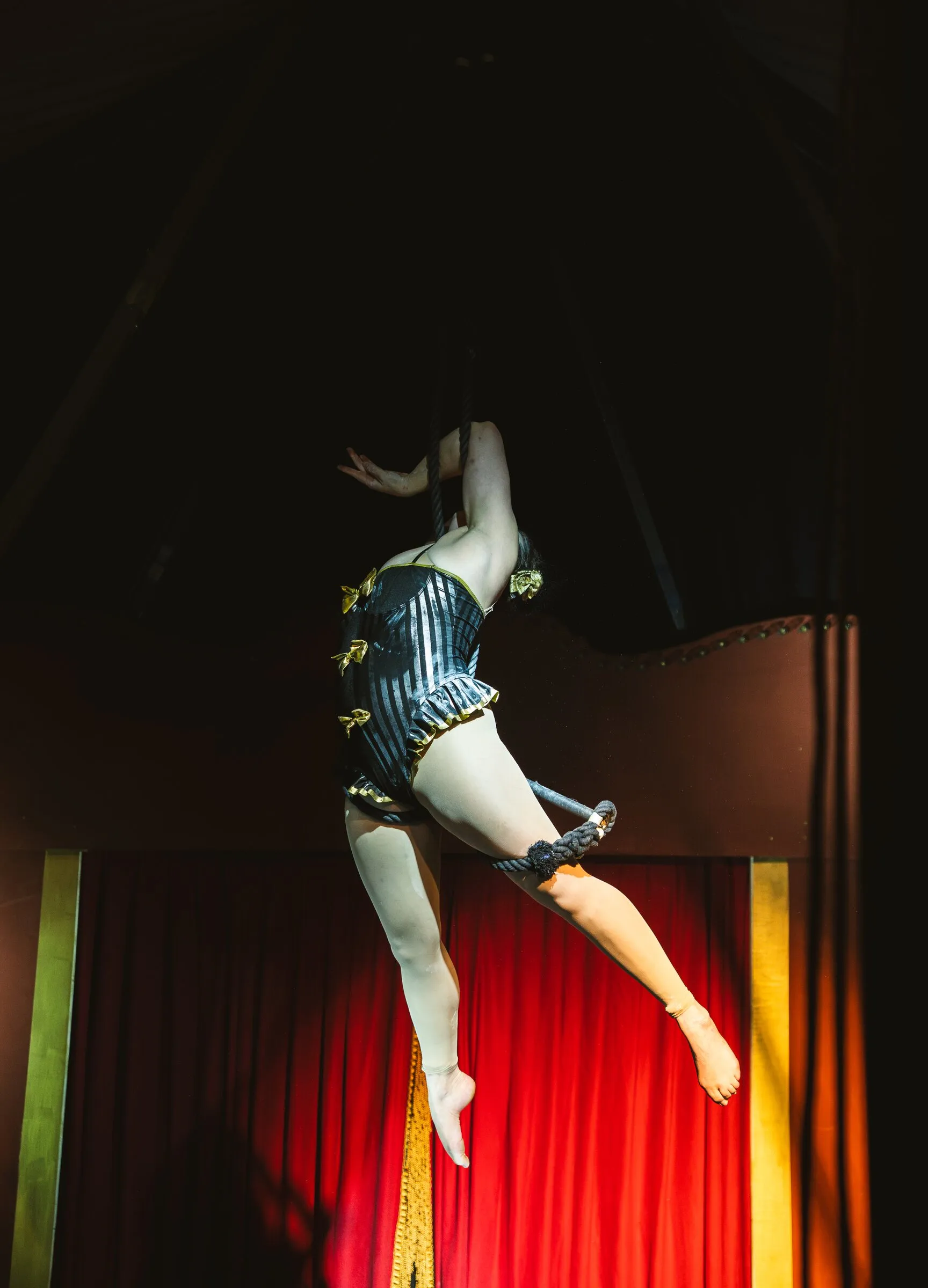 A Kuroneko Circus trapeze artist in a striped corset swinging out from the dance trapeze