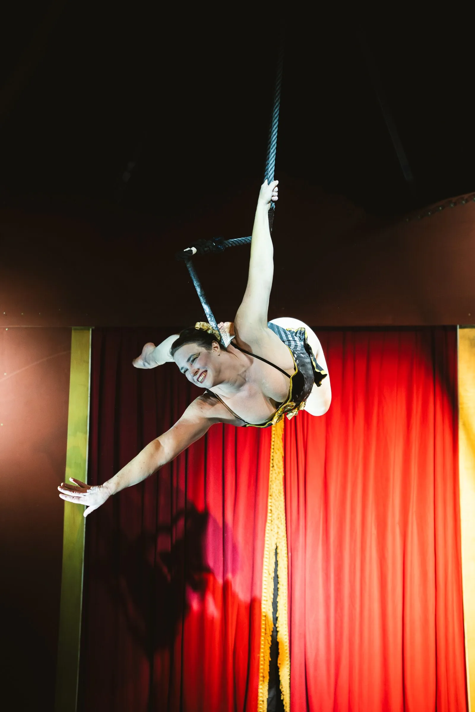 A Kuroneko Circus trapeze artist swinging out from the dance trapeze by one arm
