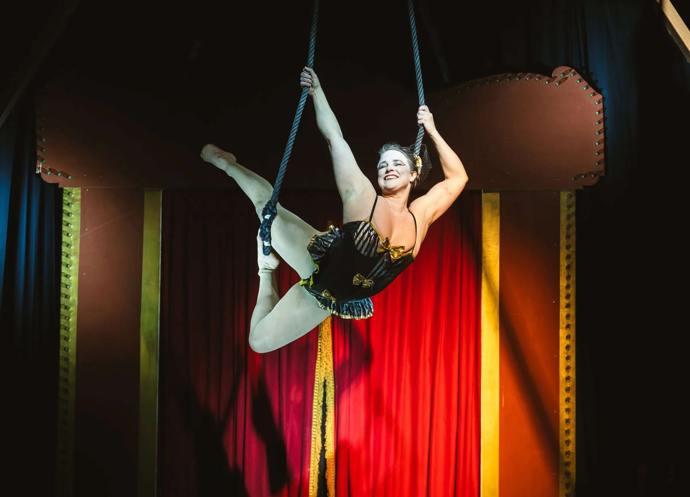 A Kuroneko Circus trapeze artist in a split mid-swing on the dance trapeze