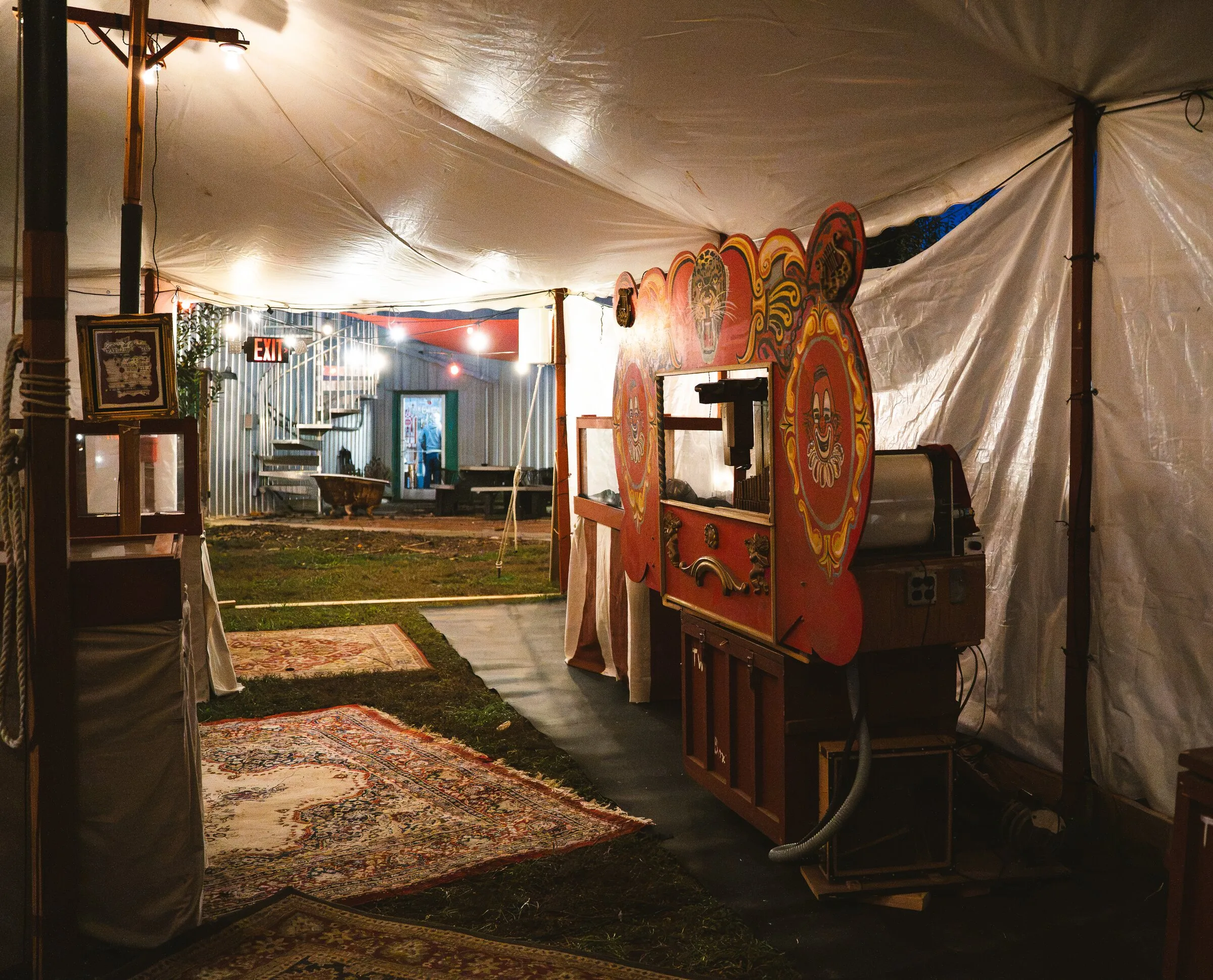 The dime museum midway inside the Kuroneko Circus tent, with a carved band organ, rugs, and lantern light