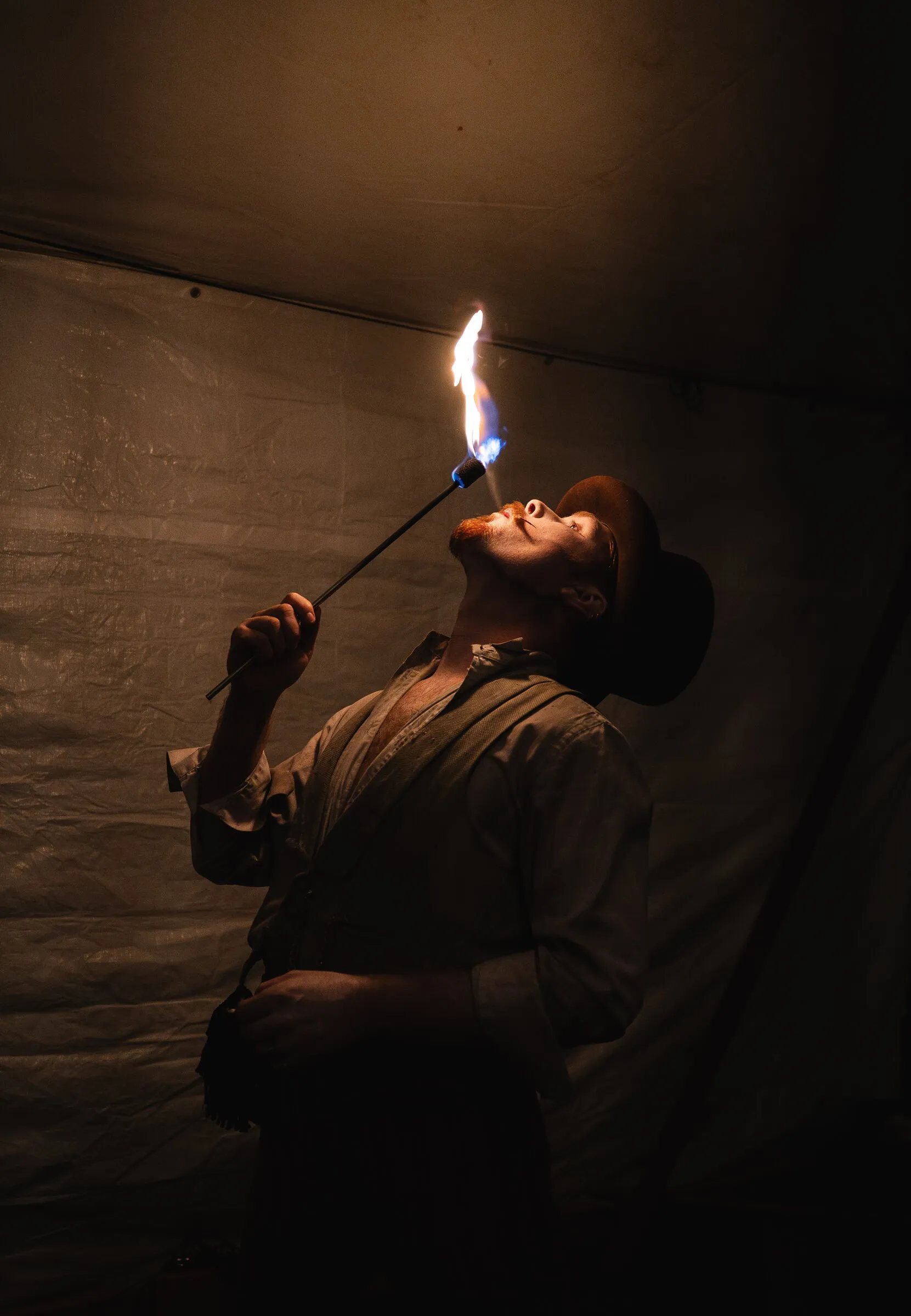 A Kuroneko Circus fire eater in a bowler hat tipping his head back to take a flaming torch