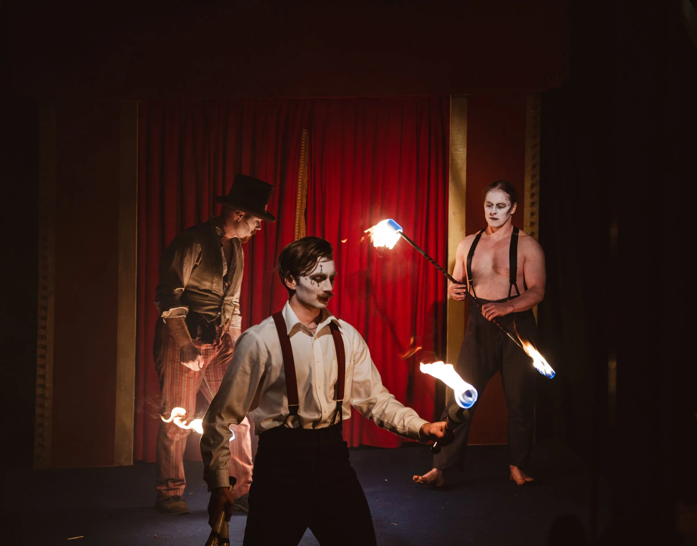 Three Kuroneko Circus performers in whiteface juggling and twirling fire on stage