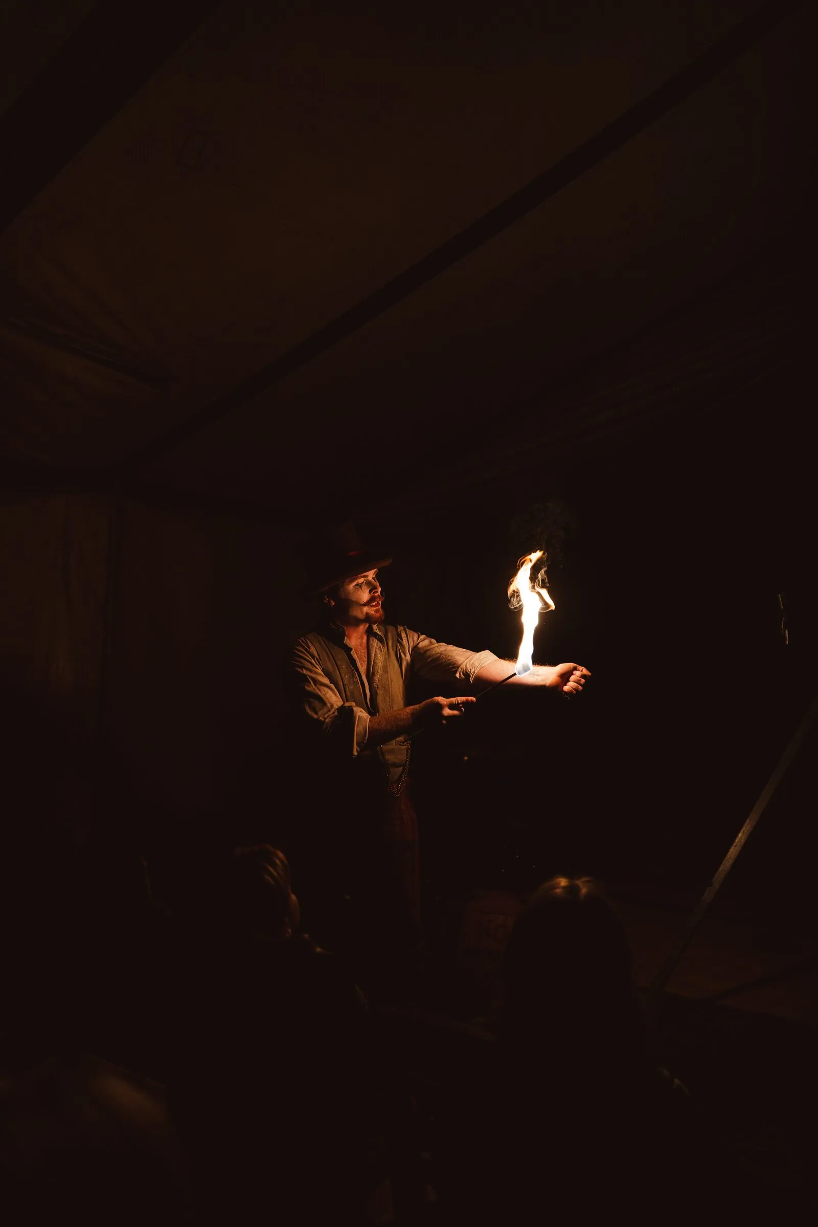 A Kuroneko Circus fire performer holding a flame on his palm before a darkened audience