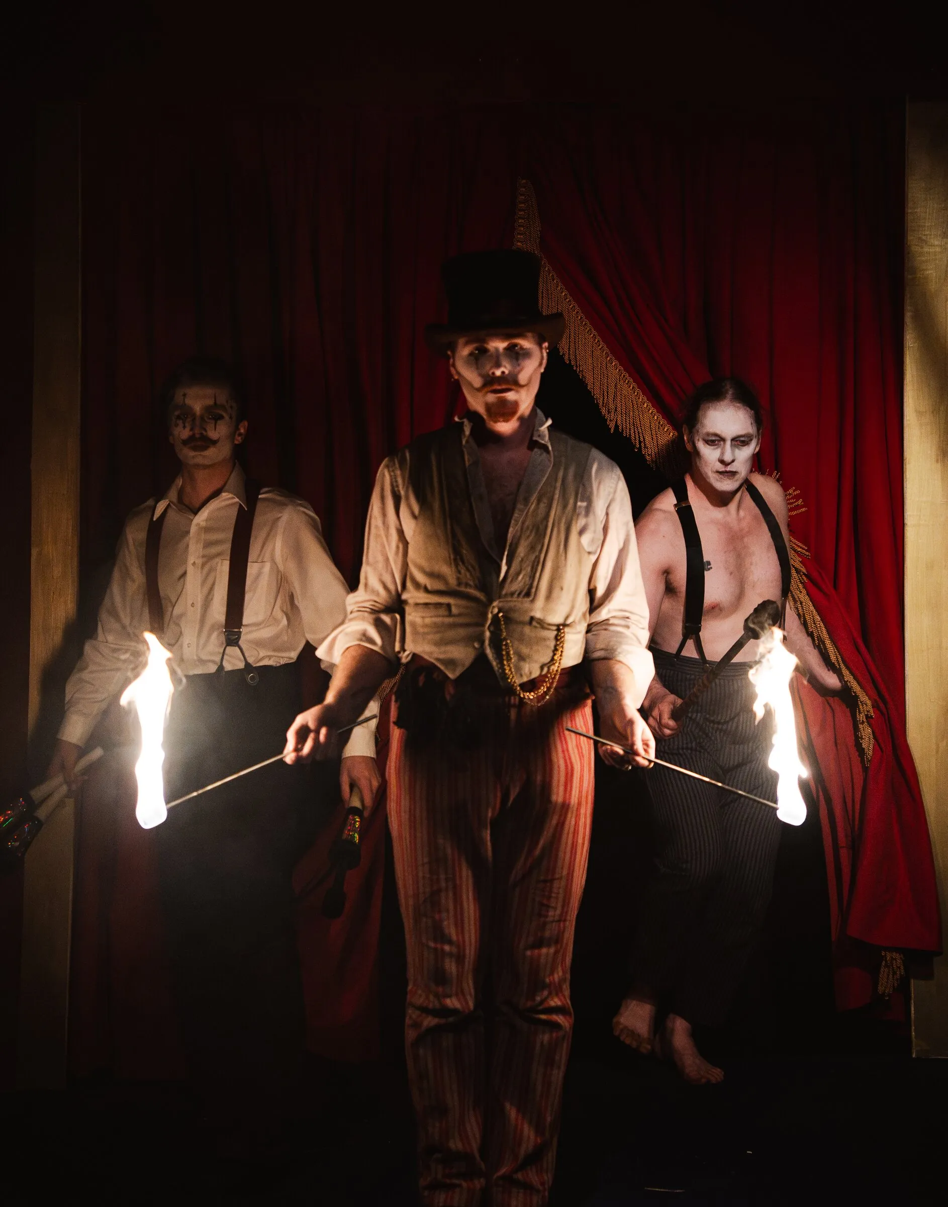 Three Kuroneko Circus fire performers stepping through the curtain holding lit torches under the big top in North Carolina