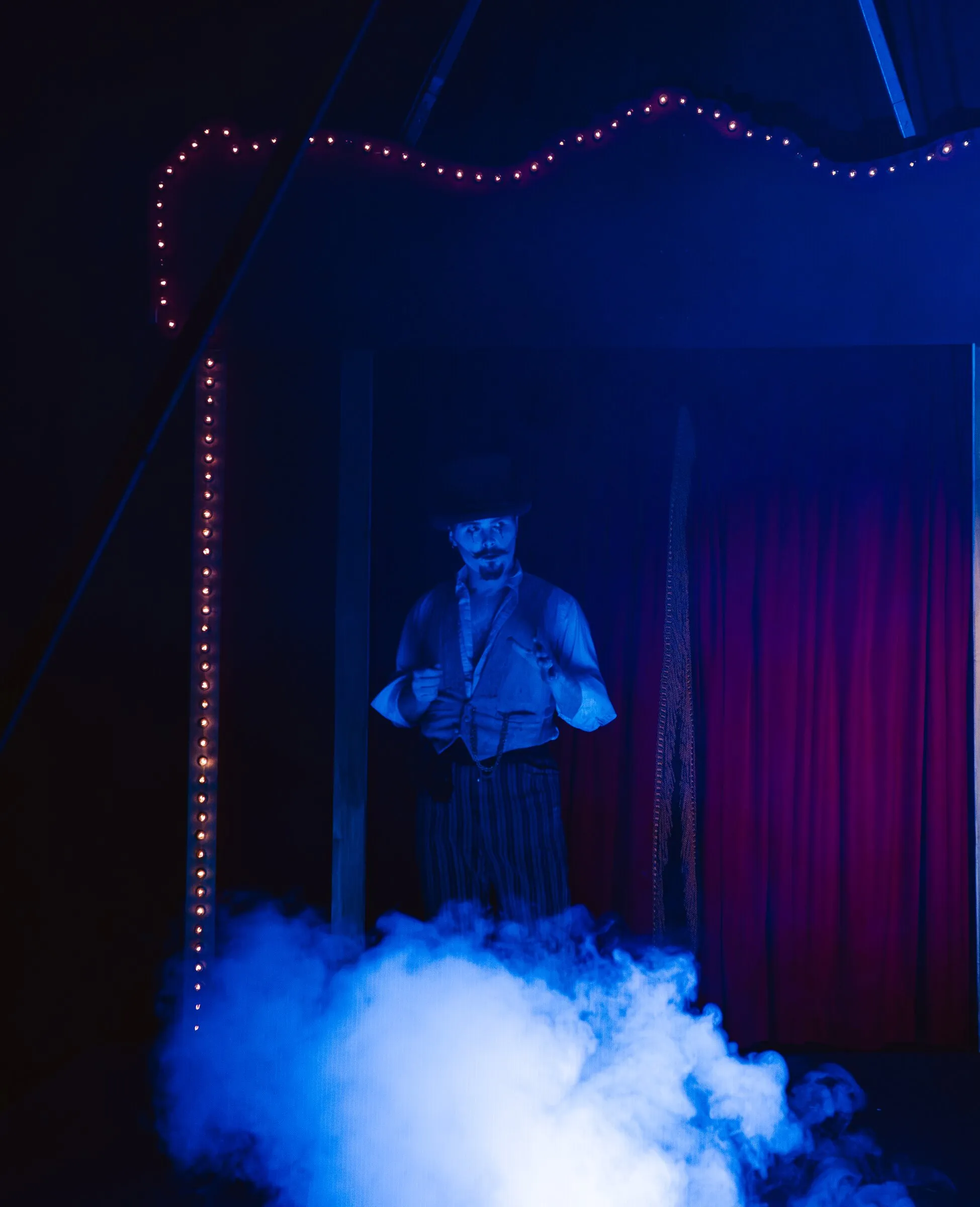 The Kuroneko Circus ringmaster rising out of blue fog beneath the lit stage arch