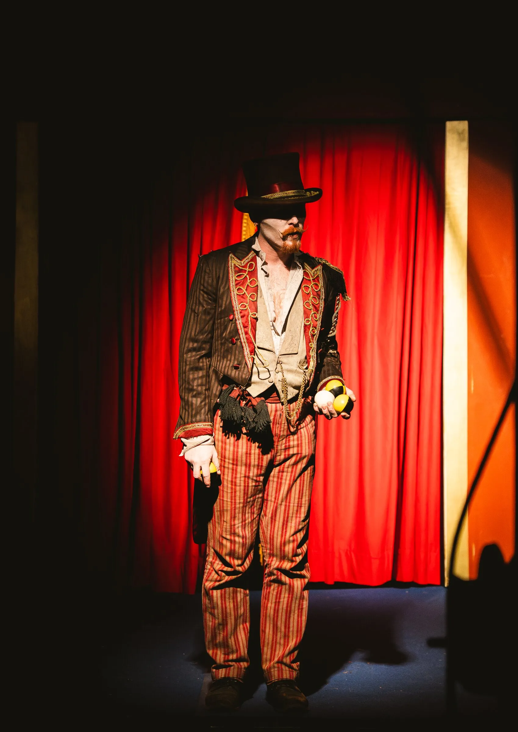 The Kuroneko Circus ringmaster in a top hat and striped trousers standing in a red spotlight